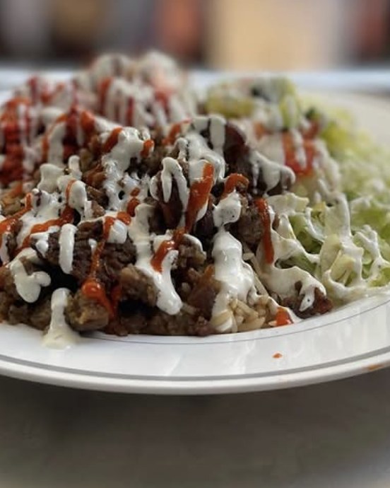 A gyro rice plate with salad, tzatziki and hot sauce